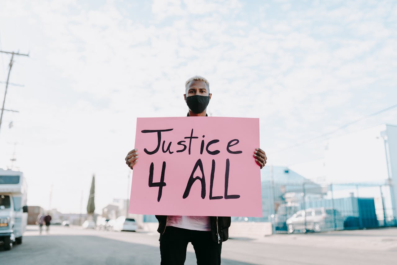gallery-2 Man holding a 'Justice 4 All' sign while wearing a face mask during an outdoor protest.