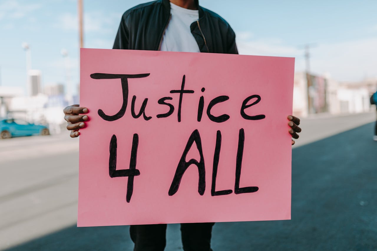 gallery-1 A protester holds a pink 'Justice 4 All' placard on an urban street.