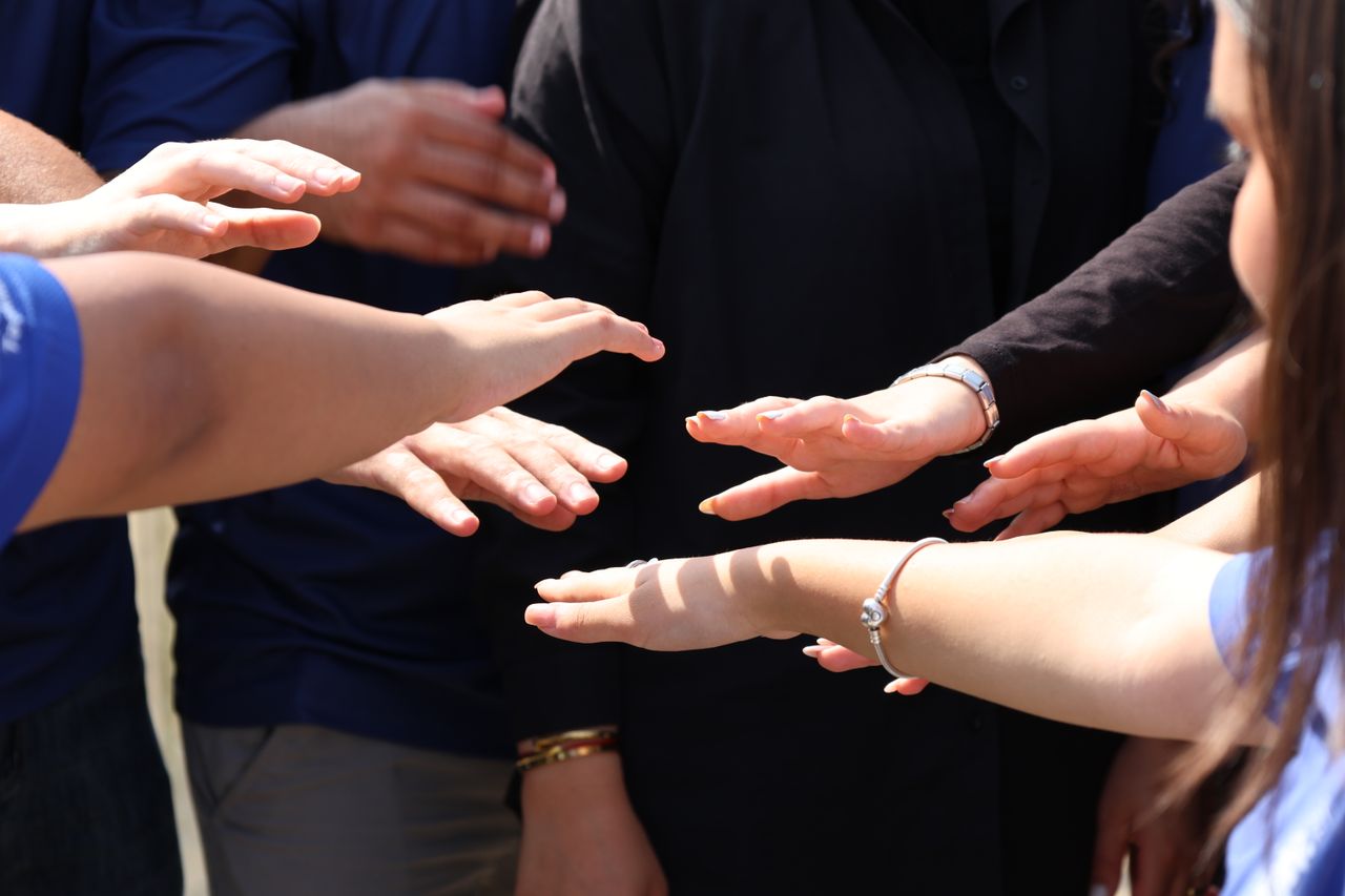 gallery-1 A diverse group of people placing hands together symbolizing teamwork and unity.