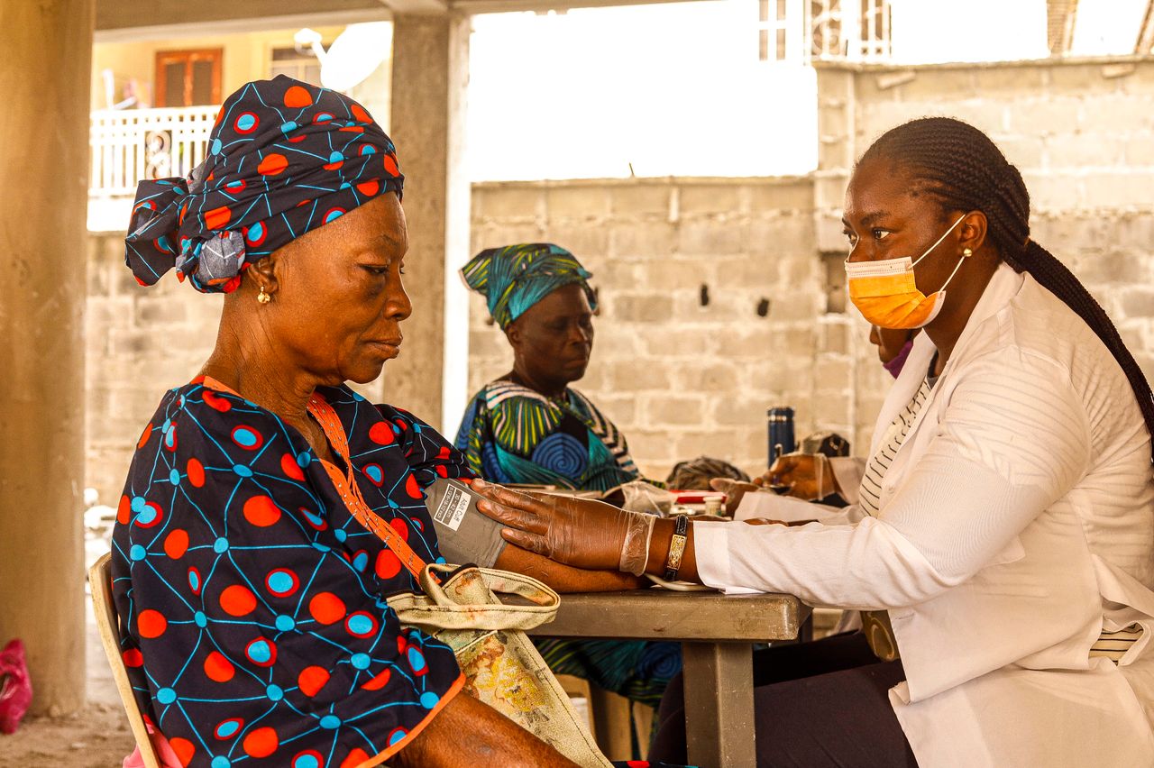 hero-img-02 A healthcare worker checks blood pressure of an elderly woman in a rural clinic setting.