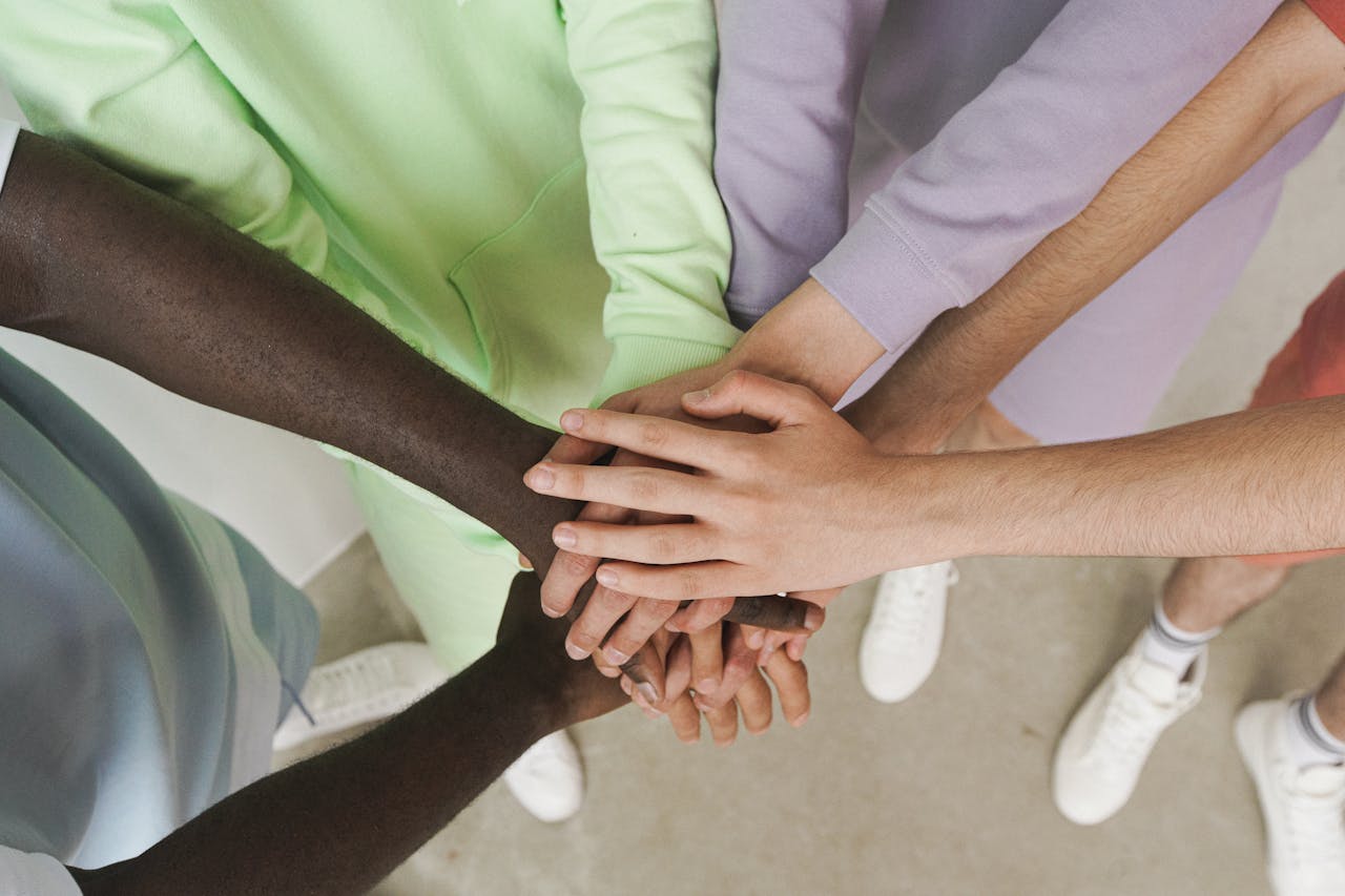 gallery-2 Top view of diverse hands stacked together, symbolizing unity and teamwork.